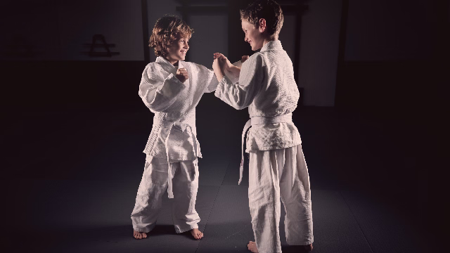 Dos niños practicando una técnica de defensa personal en un fondo negro de estudio durante una clase en Madrid
