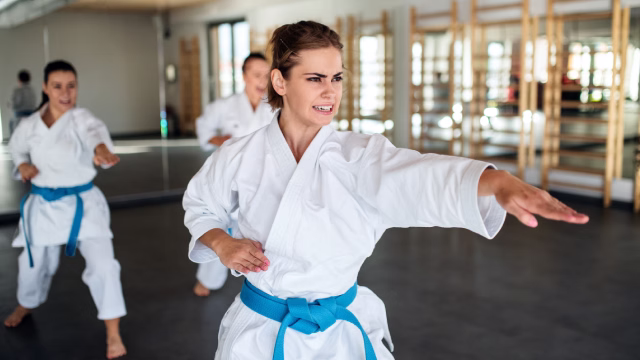 Tres mujeres adultas practicando una posición de kárate en una sala con tatami y espejos en Madrid