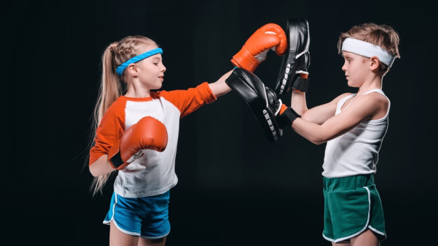 Dos niños chocando los guantes durante una clase de kickboxing infantil en una escuela y academia en Madrid con fondo negro profesional
